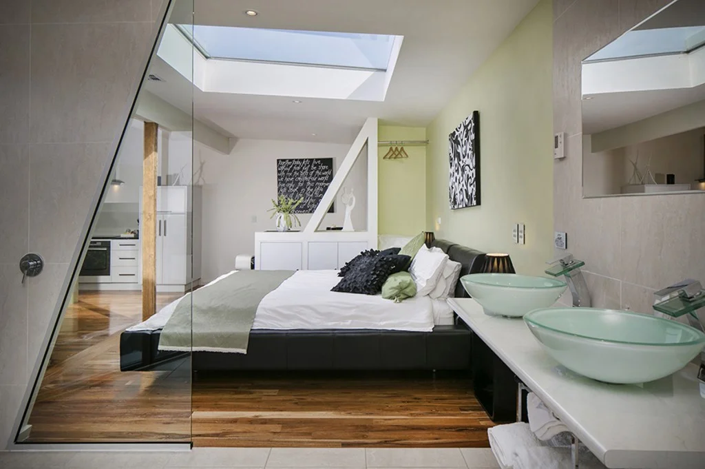 Contemporary loft-style bedroom with skylight, glass ensuite, platform bed and modern amenities featuring natural timber and stone elements