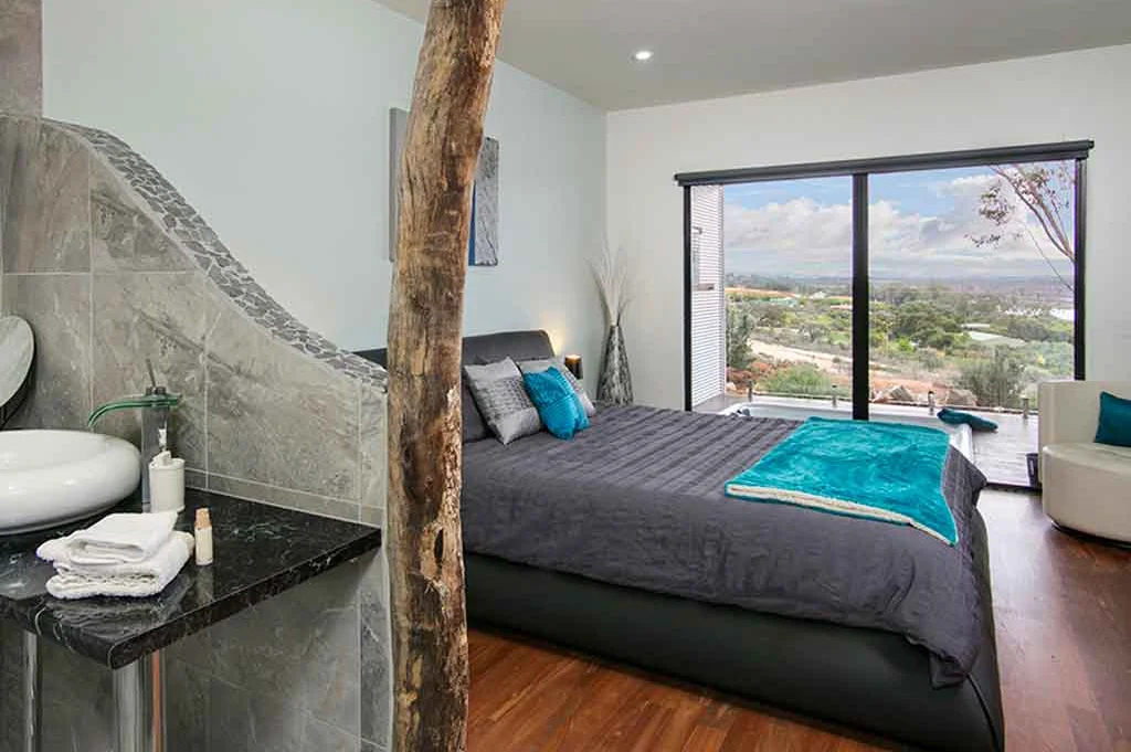 Modern bedroom with natural timber feature wall, ensuite bathroom, river valley views and sustainable design elements including recycled materials