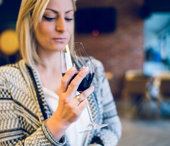 Young blonde woman holding a glass of red vine looking at beverage at party home or restaurant celebration holiday